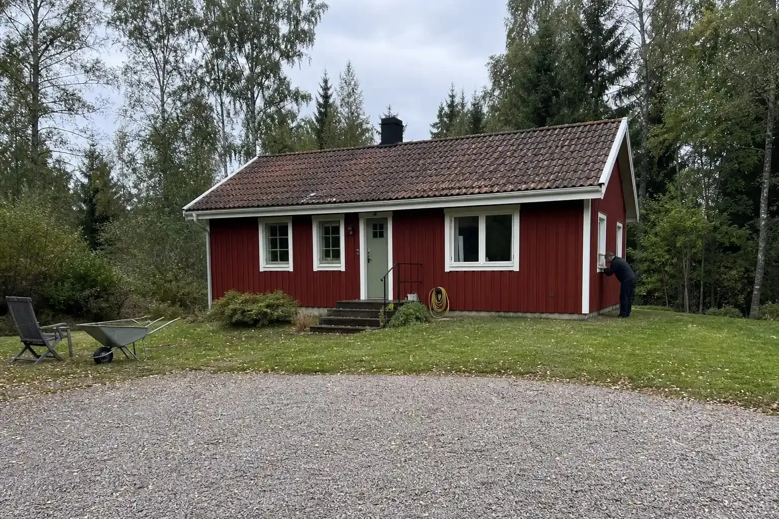 Rött fritidshus med vita knutar omgivet av träd